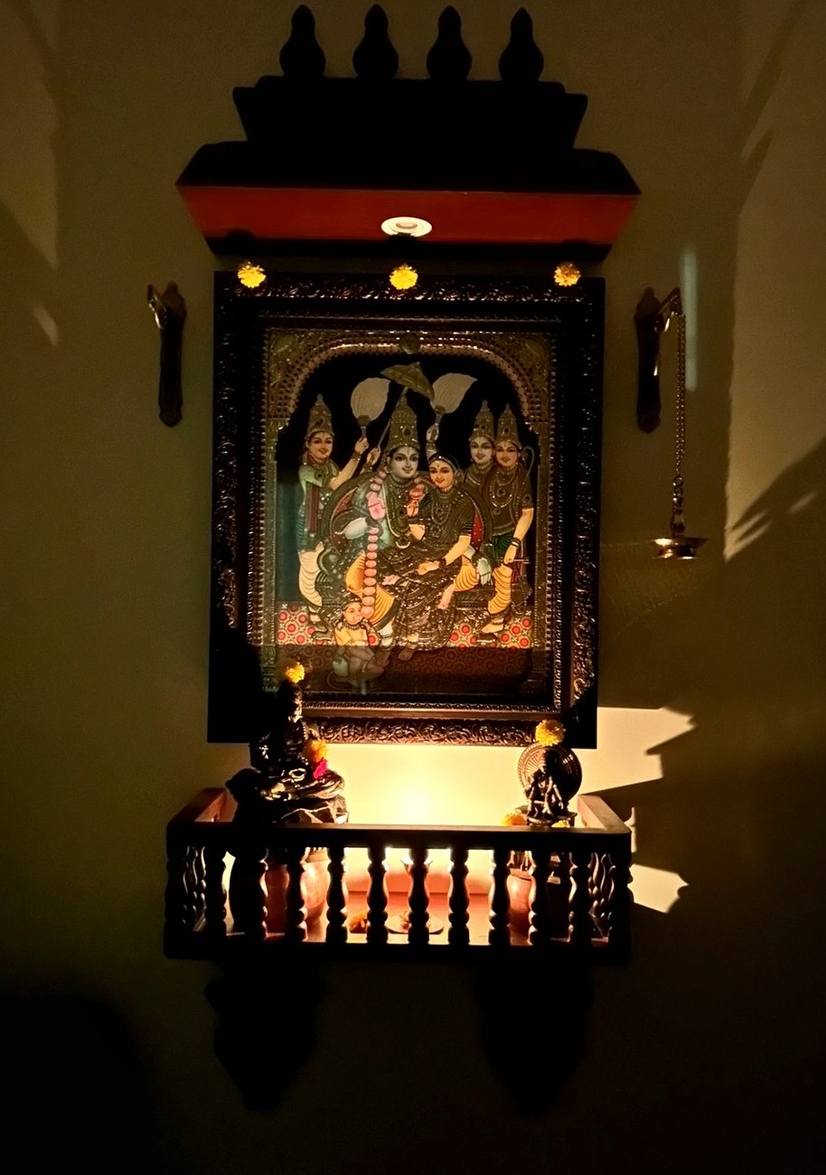 A carved pooja mandir lit with lamps in a customer's home