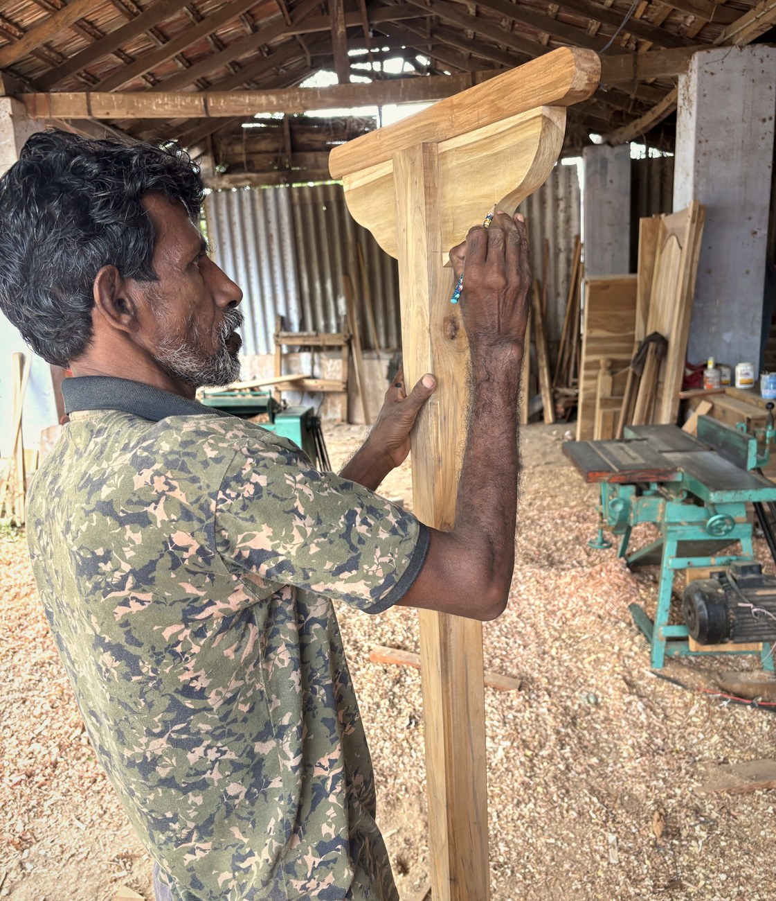 A carpenter marking out a console frame in the thatched workshop
