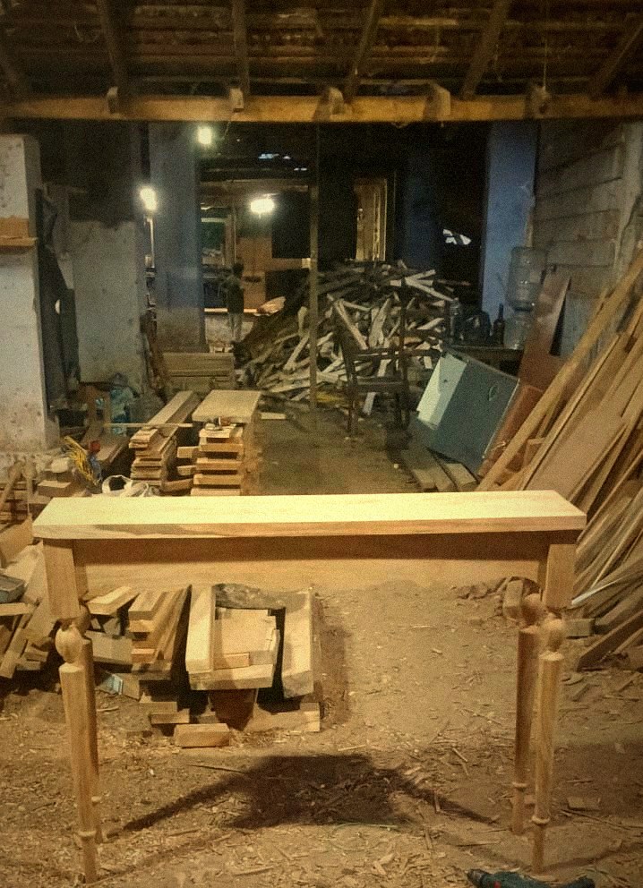 The Annam Woodworks workshop, with teak planks stacked and a console frame taking shape
