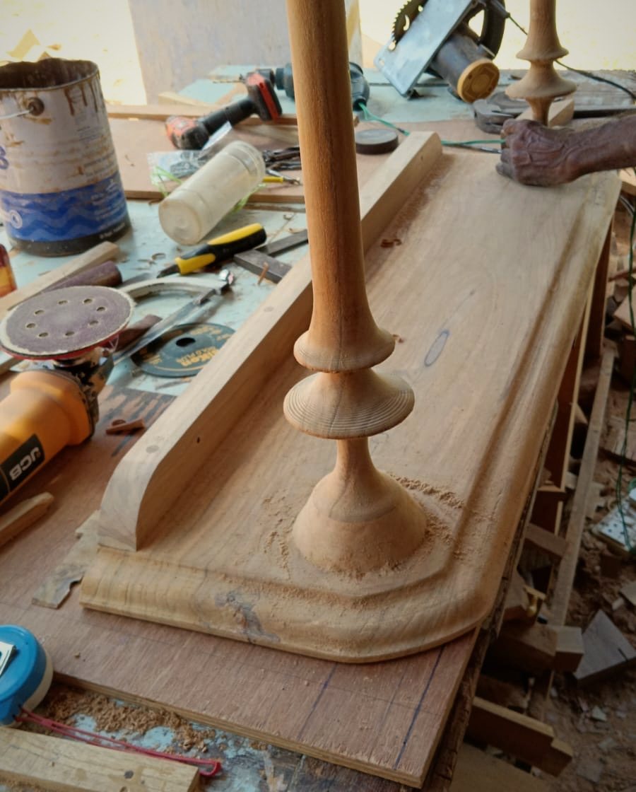Hand-turned teak legs being fitted to a console top in the workshop
